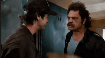 Two Men Are Standing Next To Each Other In Front Of A Door . One Of The Men Is Wearing A Hat . GIF