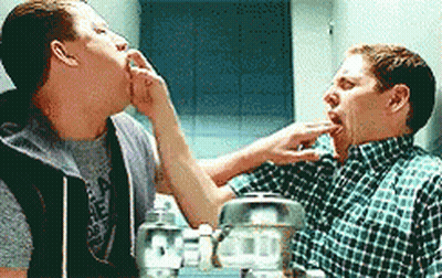 Two Men Are Standing Next To Each Other In Front Of A Mirror And One Of Them Is Licking The Other 'S Face . GIF