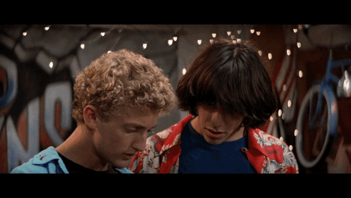 Two Men Are Standing Next To Each Other In Front Of A Sign That Says ' Riders ' On It GIF