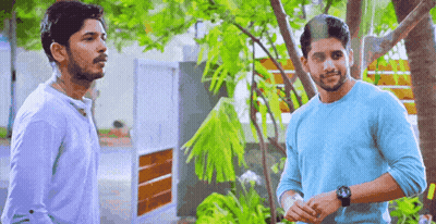 Two Men Are Standing Next To Each Other In Front Of A Tree Talking To Each Other . GIF