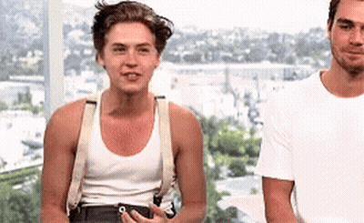 Two Men Are Standing Next To Each Other In Front Of A Window . One Of The Men Is Wearing Suspenders And A Tank Top . GIF