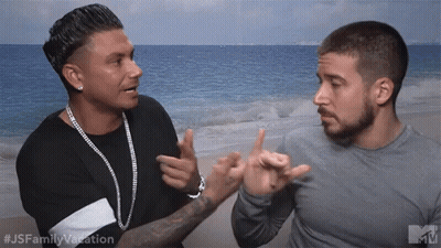 Two Men Are Standing Next To Each Other On A Beach And One Is Pointing At The Other 'S Face . GIF