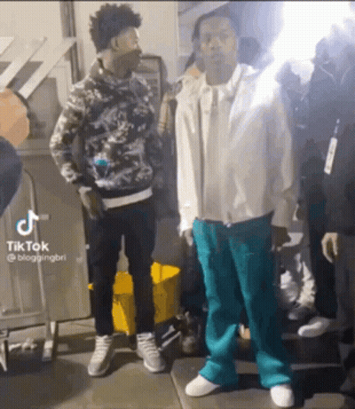Two Men Are Standing Next To Each Other On A Sidewalk And Talking To Each Other . GIF