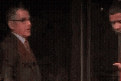 Two Men Are Standing Next To Each Other On A Stage In A Dark Room . GIF