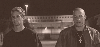Two Men Are Standing Next To Each Other On A Street At Night . One Of The Men Is Wearing A Cross Necklace . GIF