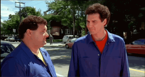 Two Men Are Standing Next To Each Other On A Street Talking GIF