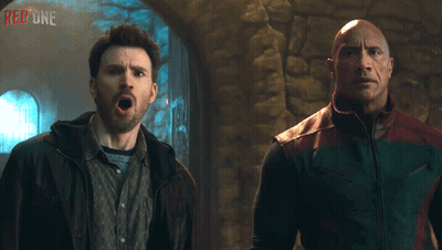 Two Men Are Standing Next To Each Other With The Word Red One On The Wall Behind Them GIF