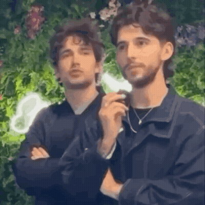 Two Men Are Standing Next To Each Other With Their Arms Crossed And Looking At Something . GIF