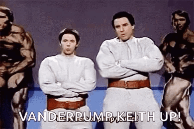 Two Men Are Standing Next To Each Other With Their Arms Crossed In Front Of A Group Of Muscular Men . GIF