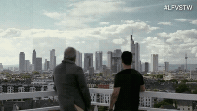 Two Men Are Standing On A Balcony Looking At A City Skyline With The Hashtag #Lfvstw GIF