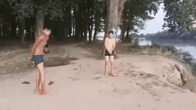 Two Men Are Standing On A Sandy Beach Next To A River . GIF