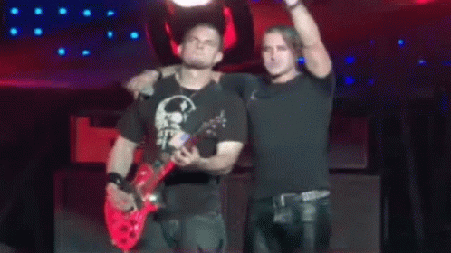 Two Men Are Standing On A Stage With One Holding A Red Guitar GIF