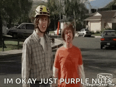 Two Men Are Standing On A Street And One Of Them Is Wearing A Helmet And The Other Is Wearing An Orange Shirt GIF