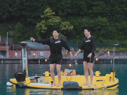 Two Men Are Standing On A Yellow Boat With The Number 80015 On It GIF