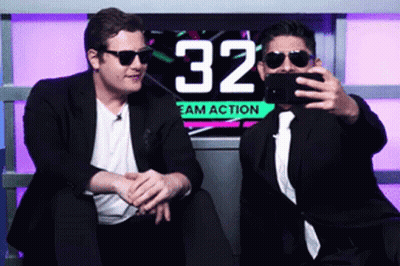 Two Men Are Taking A Selfie In Front Of A Sign That Says 32 GIF