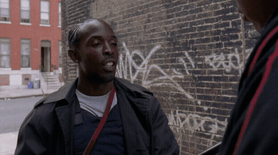 Two Men Are Talking In Front Of A Brick Wall That Has Graffiti On It GIF
