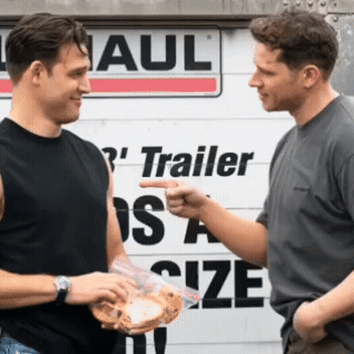 Two Men Are Talking In Front Of A Trailer Size Sign GIF