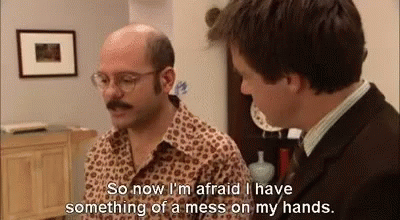 Two Men Are Talking To Each Other In A Living Room . One Of The Men Is Bald And Has A Mustache . GIF