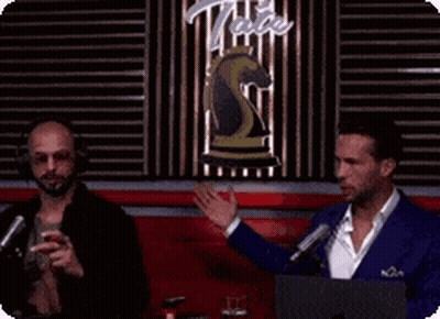 Two Men Are Talking To Each Other In Front Of A Sign That Says Tate GIF