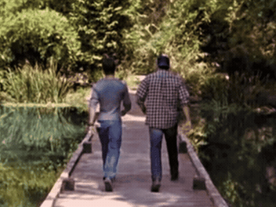 Two Men Are Walking Across A Wooden Bridge GIF
