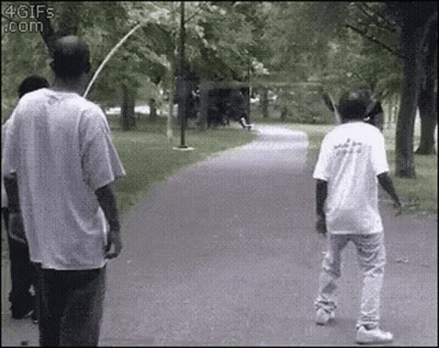 Two Men Are Walking Down A Path In A Park . One Of The Men Is Holding A Bat . GIF