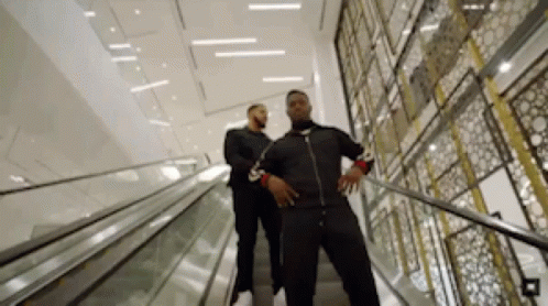 Two Men Are Walking Down An Escalator In A Building . GIF