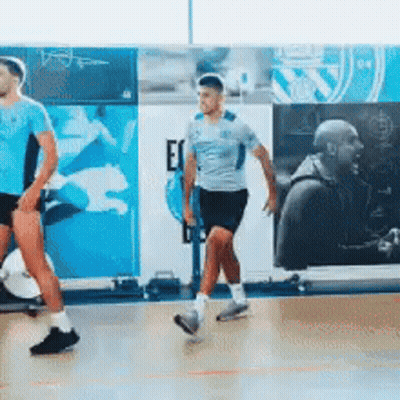 Two Men Are Walking On A Basketball Court In Front Of A Wall That Says Ec On It GIF