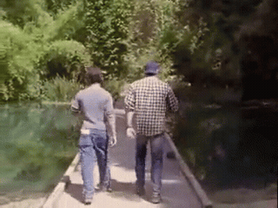 Two Men Are Walking On A Bridge Over A River . GIF