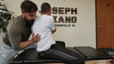 Two Men Are Working On A Man 'S Back In Front Of A Sign That Says Joseph Tano Reenville Sc GIF