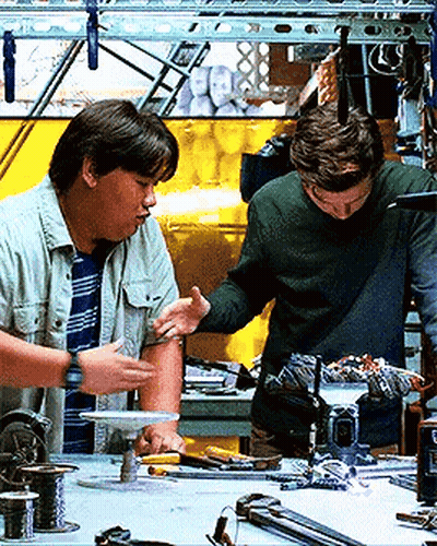 Two Men Are Working On A Project In A Workshop And One Of Them Is Touching Another Man 'S Arm GIF