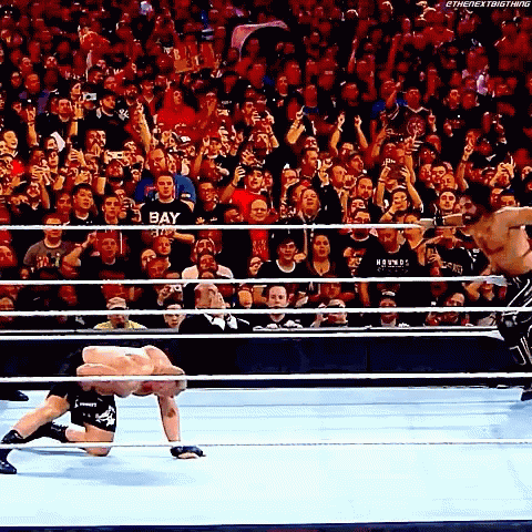 Two Men Are Wrestling In A Ring With A Crowd Watching And One Of The Men Is Wearing A Shirt That Says Bay GIF