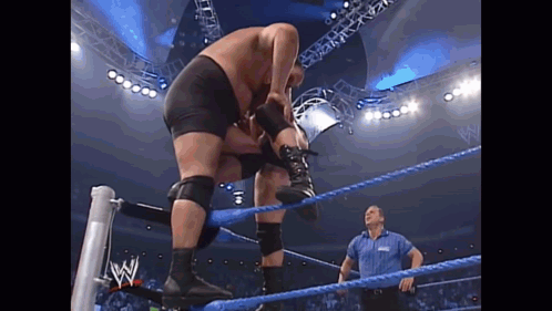 Two Men Are Wrestling In A Wrestling Ring While A Referee Looks On . GIF