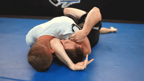 Two Men Are Wrestling On A Blue Mat And One Of Them Is Wearing A Shirt That Says " Ufc " GIF