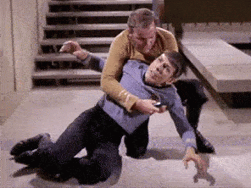 Two Men Are Wrestling On The Floor In A Room With Stairs In The Background . GIF