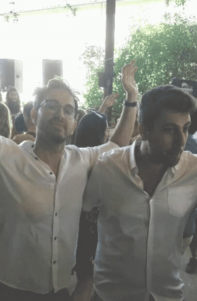 Two Men Arms Outstretched In Crowd With Corona Sign GIF
