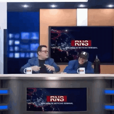 Two Men At Desk In Front Of RNS Resumen De Noticias Semanal Screen GIF