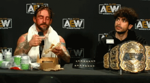 Two Men At Table In Front Of AEW Wrestling Wall GIF