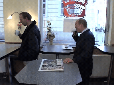 Two Men At Table In Front Of Bakery Sign GIF