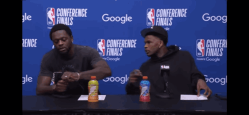 Two Men At Table In Front Of Conference Finals Sign GIF