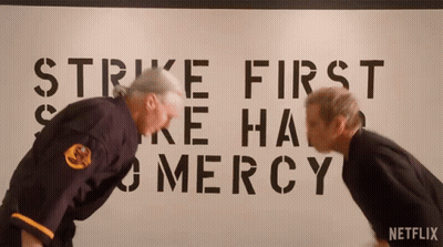 Two Men Bending Over In Front Of Strike First And Mercy Sign GIF