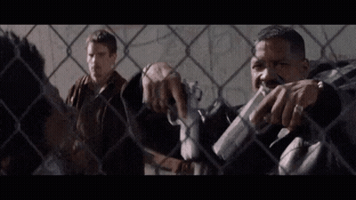 Two Men By Chain Link Fence, One With Gun GIF