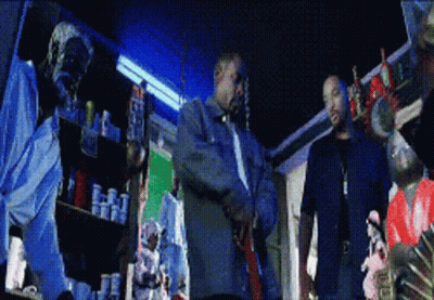 Two Men By Shelf Full Of Bottles GIF