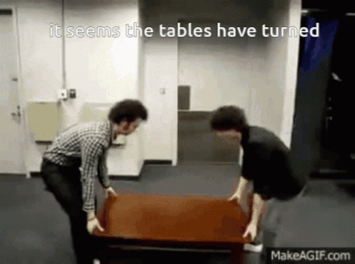 Two Men Carrying A Table That Says It Seems The Tables Have Turned On Makeagif.com GIF