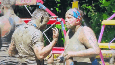 Two Men Covered In Mud Are Standing Next To Each Other In A Muddy Field . GIF