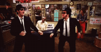 Two Men Dancing In Front Of A Help Wanted Sign GIF