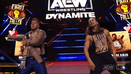 Two Men Dancing In Front Of Dynamite Wrestling Sign GIF