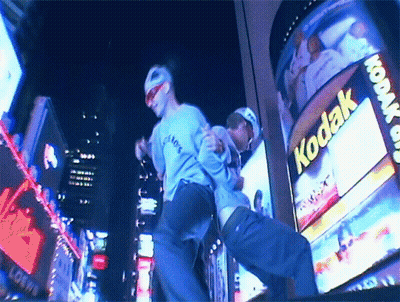 Two Men Dancing In Front Of Kodak Billboard GIF