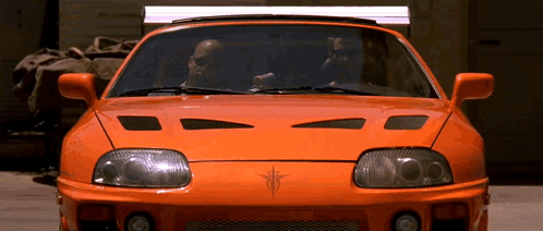 Two Men Driving Orange Sports Car In Garage GIF