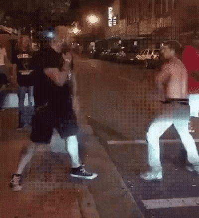 Two Men Fighting On Sidewalk In Front Of Building GIF