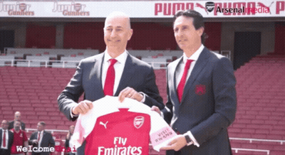 Two Men Holding Fly Emirates Jersey In Front Of Puma Banner GIF